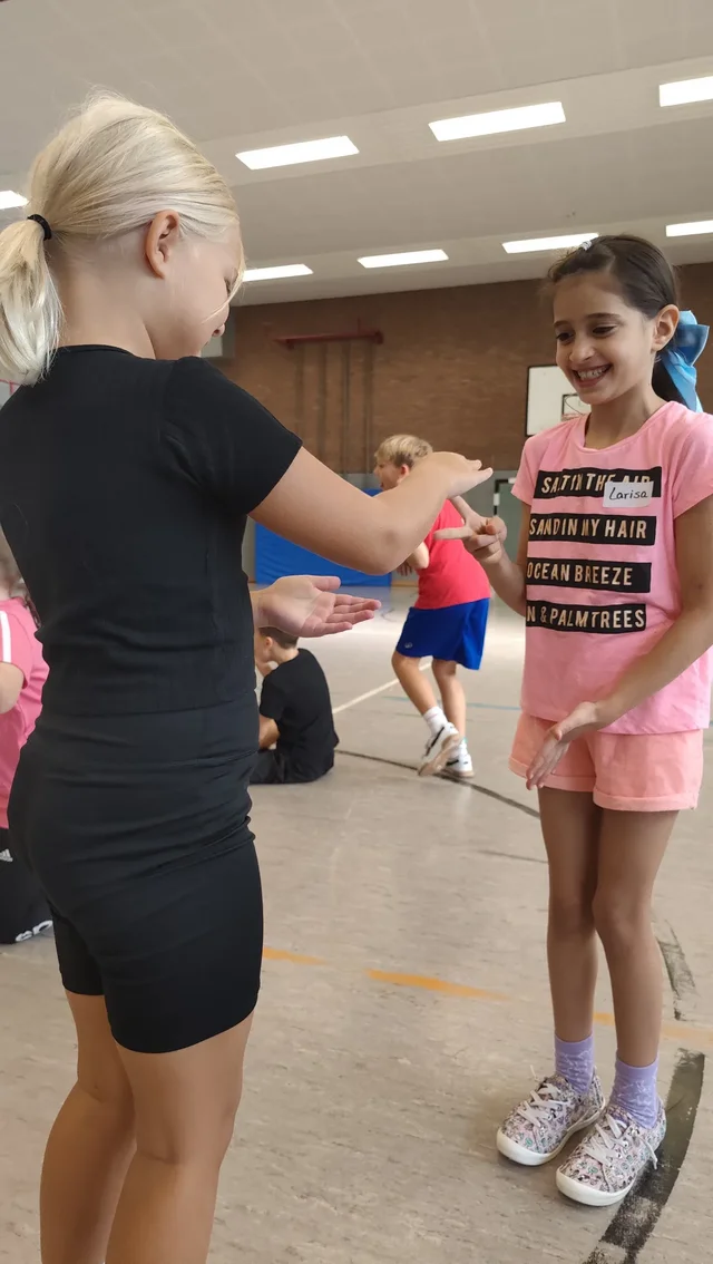 Kinder üben paarweise in der Sporthalle Zusammenarbeit.