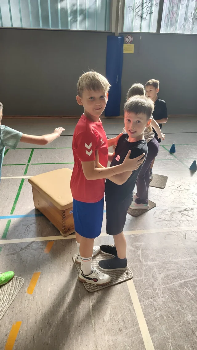 Kinder meistern in der Sporthalle eine gemeinsame Bewegungsaufgabe.