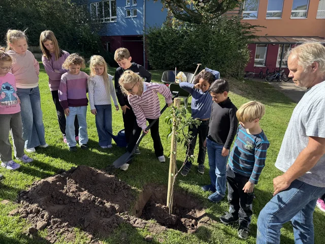 Kinder und Erwachsene stehen um den frisch gepflanzten Birnbaum.