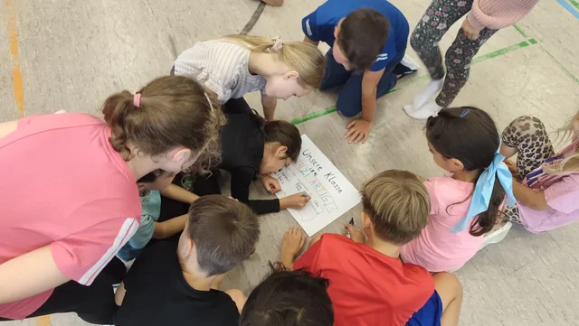 Kinder lösen am Boden gemeinsam eine Teambuilding-Aufgabe.