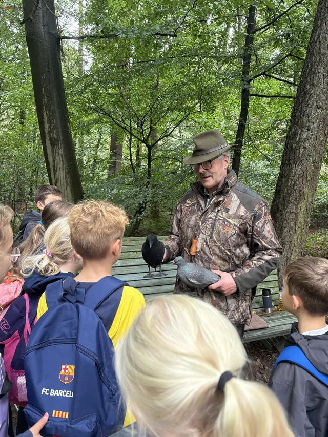 Fachperson erklärt Schülerinnen und Schülern eine Station im Wald.