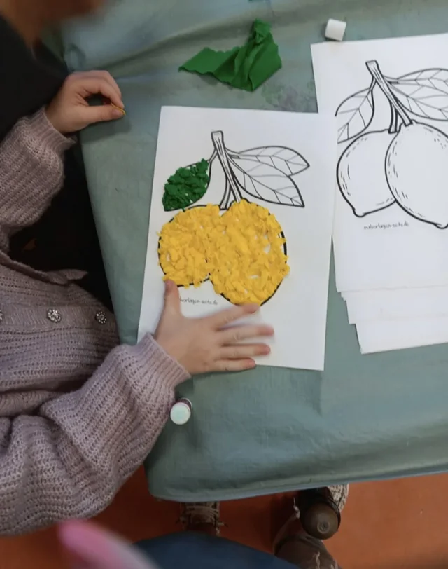 Kind gestaltet ein Mosaikbild mit kleinen Papierschnipseln.