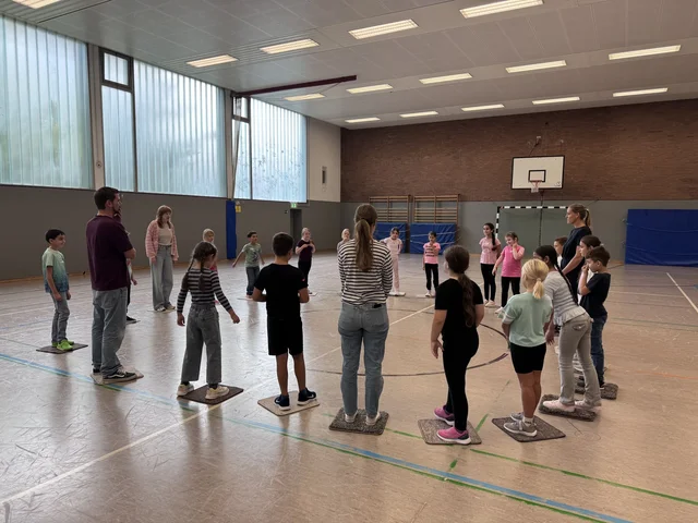 Schülerinnen und Schüler nehmen an einer Gruppenübung in der Sporthalle teil.